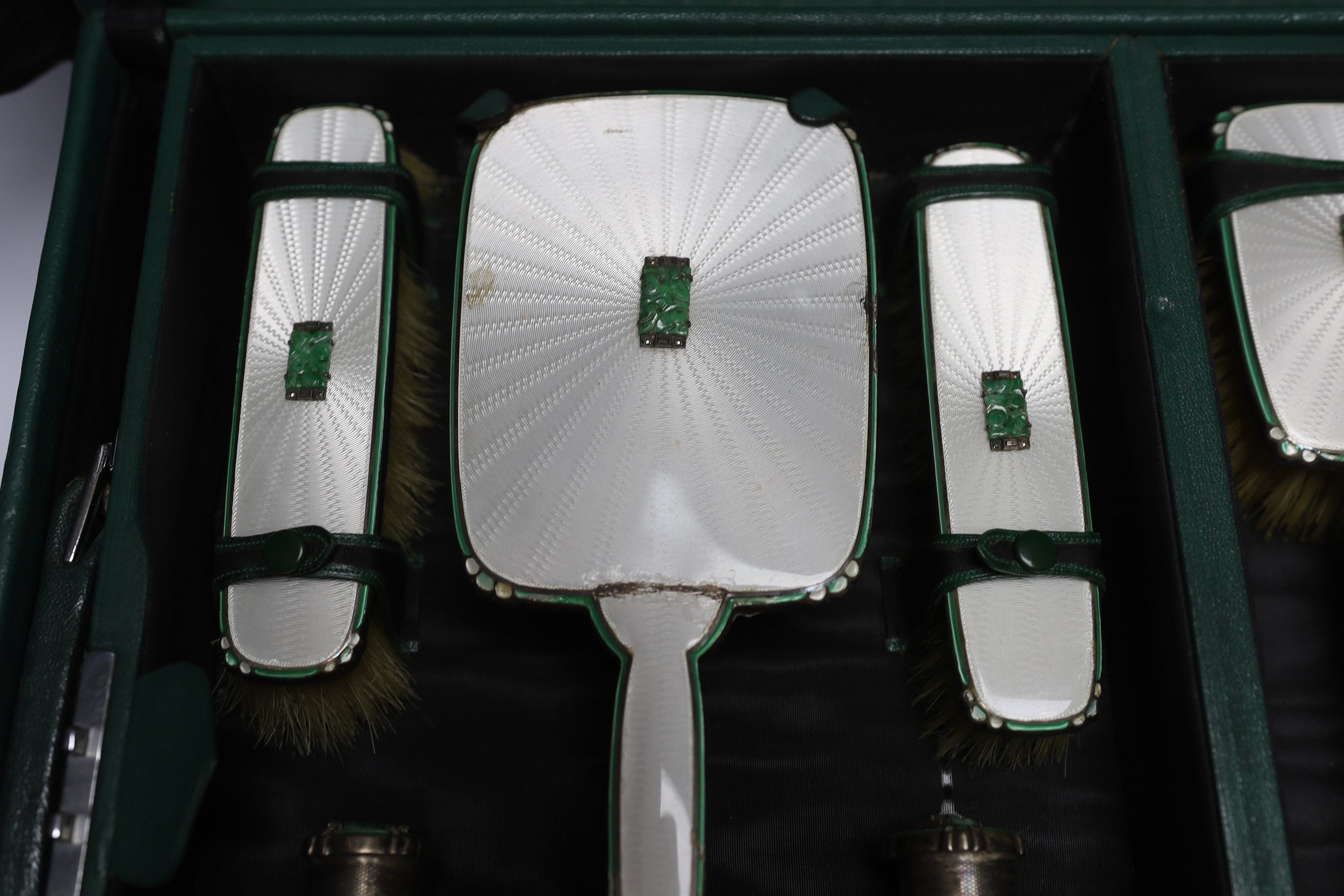 A George V silver, enamel and Chinese jadeite mounted twelve piece dressing table set, Goldsmiths & Silversmiths Co Ltd, Birmingham, 1936, housed in green leather travelling case, case width 53cm (a.f.).